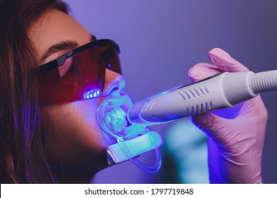 Close-up portrait of a female patient at dentist in the clinic. Teeth whitening procedure with ultraviolet light UV lamp.