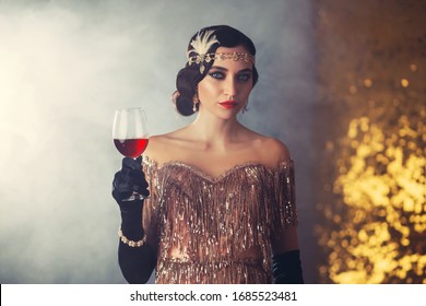 Closeup Portrait Flapper Woman With Glass Wine. Holiday Headband Finger Wave Hairstyle, Vintage Style 20s Dress Evening Makeup Red Lips Smokey Cat Eyes. Backdrop Golden Room Smoke. Elegant Prom Image