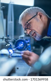 Close-up Portrait Of Focused Middle Aged Engineer In Glasses Working With High Precision Laser Equipment, Using Lenses And Testing Optics For Accuracy Required Electronics