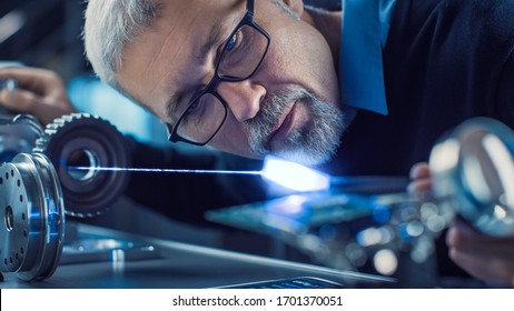 Close-up Portrait Of Focused Middle Aged Engineer In Glasses Working With High Precision Laser Equipment, Using Lenses And Optics For Accuracy Electronics. Testing Superconductor Material