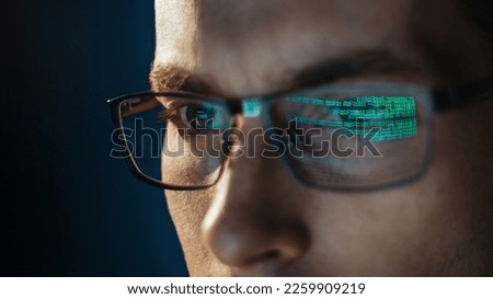 Close-up portrait of focused software engineer wearing eyeglasses looking at computer screen working with big data. Programming code reflecting in glasses. Data science, Machine Learning, AI concept