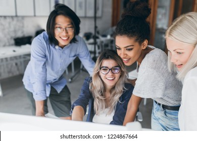 Close-up portrait of freelance it-specialists looking at laptop screen with smile. Asian programmer in glasses helping to black girl in white t-shirt with her project.