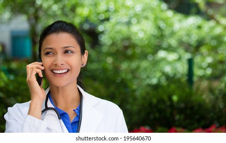 Closeup Portrait, Friendly, Young Smiling Confident Female Doctor, Healthcare Professional Talking On Phone, Isolated Outside Green Trees Background. Patient Visit Health Care Reform. Positive Emotion