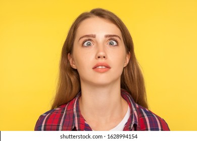 Closeup portrait of funny silly ginger woman in checkered shirt looking up cross eyed with stupid dumb face, girl has awkward confused comical expression. studio shot isolated on yellow background