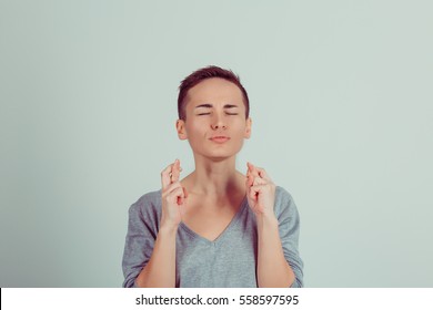 Closeup portrait of a girl short hair style boy alike woman with fingers crossed gesture eyes closed wishing for better future isolated on a green white background. Horizontal studio shot
