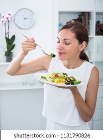 closeup portrait of glad young woman holding plate with green salad indoors