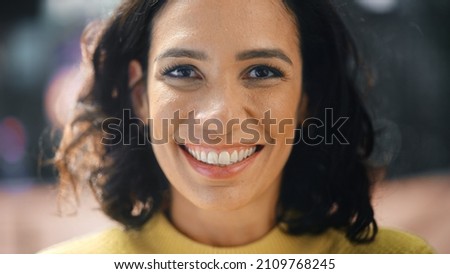 Close-up Portrait of Gorgeous Dark Haired Hispanic Woman with Deep Brown Eyes Looking at Camera, Smiling Charmingly. Happy Young Latin Woman Enjoys Life with Fun, Success. Background Bokeh City Street