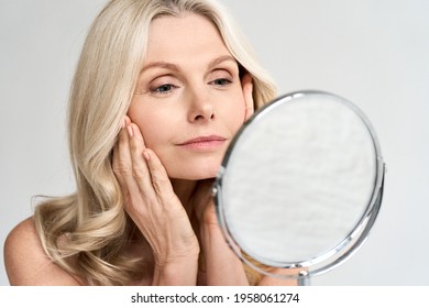 Closeup portrait of gorgeous happy middle age woman looking at mirror touching her skin enjoying treatment for dry skin. Advertising of antiaging beauty skin care products. - Shutterstock ID 1958061274
