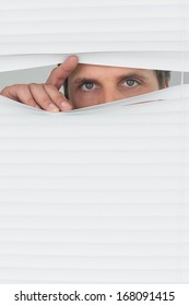 Close-up portrait of a green eyed businessman peeking through blinds in the office