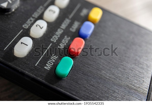 A closeup portrait of the green movie sound\
mode button on a television remote control. There are other colored\
mode buttons on the device.