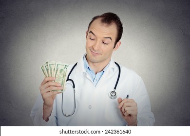 Closeup portrait grumpy greedy miserly health care professional, male doctor holding, protecting his money dollars in hand isolated grey wall background. Negative human emotions, facial expressions