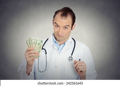 Closeup portrait grumpy greedy miserly health care professional, male doctor holding, protecting his money dollars in hand isolated grey wall background. Negative human emotions, facial expressions