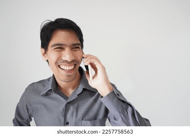 Closeup portrait of handsome Asian man happy talking on mobile phone, looking to copy space side, isolated grey background. Concept of happy business person, attractive male in wireless communication. - Shutterstock ID 2257758563