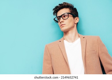 Closeup Portrait Of Handsome Confident Stylish Hipster Lambersexual Model. Sexy Modern Man Dressed In Elegant Beige Suit. Fashion Male Posing In Studio Near Blue Wall. In Spectacles