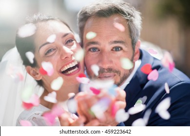 Closeup portrait of an handsome couple of newlyweds blowing confetti to camera