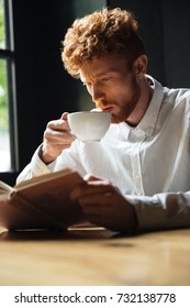 Close-up Portrait Of Handsome Curly Bearded Man Drinking Coffe While Reading Book