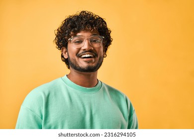 Close-up portrait of a handsome curly-haired Indian man in a turquoise t-shirt and glasses laughing and looking at the camera. - Powered by Shutterstock