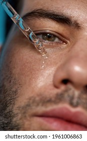 Closeup Portrait Of Handsome Guy With Smooth Skin Looking At Camera, Applying Serum Beauty Product On His Face Using Glass Pipette. Nourishing Therapy, Skin Care Concept. Vertical Shot