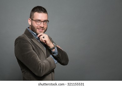 Close-up portrait of handsome hipster man in jacket smiling. Man in glasses touching his chin and looking at the camera.