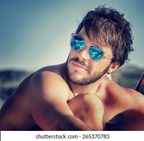 Closeup Portrait Of Handsome Man On The Beach In Mild Sunset Light, Wearing Blue Stylish Sunglasses, Summer Vacation Concept