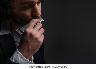 close-up portrait of handsome musician playing harmonica on black - Powered by Shutterstock