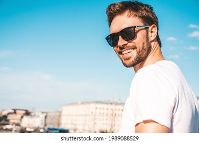 Closeup portrait of handsome smiling  hipster lambersexual model.Stylish man dressed in white T-shirt. Fashion male posing behind blue sky on the street background in sunglasses - Shutterstock ID 1989088529