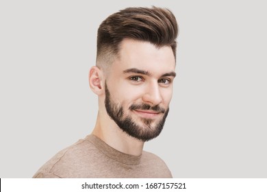 Closeup portrait of handsome smiling young man. Cheerful men isolated on gray background studio shot. Men model face with beard and modern haircut