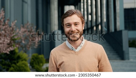 Close-up portrait of handsome success man, looking up at camera, smiling at office building background. Outdoors