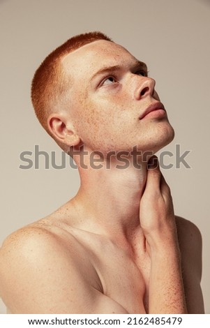 Close-up portrait of handsome young red-haired man posing isolated over grey studio background. Male natural beauty. Concept of men's health, posing, beauty, body and skin care. Thoughtful look