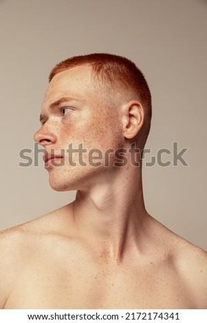 Close-up portrait of handsome young red-haired man posing isolated over grey studio background. Male natural beauty. Concept of men's health, posing, beauty, body and skin care. Model with freckles