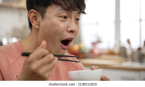 Closeup Portrait Of Happy Asian Man Giving Praise To Family About Yummy Food As He Is Taking A Bite Of Vegetable With Chopsticks During Lunch At Home