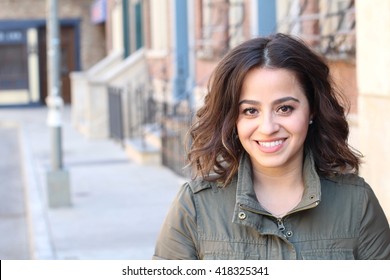 Closeup portrait, happy beautiful, smiling young woman in green jacket, posing on outdoors sidewalk, isolated on background with buildings, city urban life