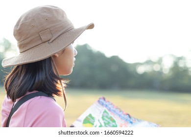 Closeup Portrait Of Happy Beautiful Young Adventurous Woman In Casual Clothes With Hat, Map Is Looking At Something, To Find Way On Map, In Forest While Walking And Hiking For Camping On Epic Mountain