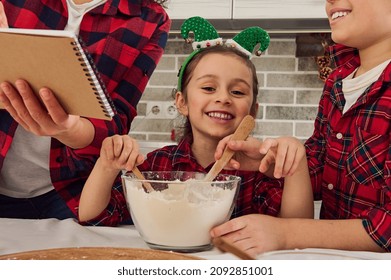 Close-up Portrait Of A Happy Cheerful Sweet Caucasian Baby Girl Smiles Toothy Smile Looking At Camera Sitting At A Kitchen Table Between Her Brother And Mom While Cooking Together Christmas Bakeries