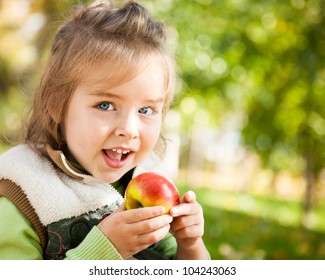 Closeup Portrait Of Happy Child Eating Red Apple Outdoors In Autumn