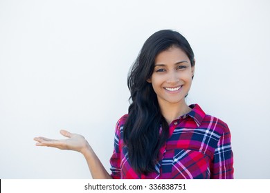 Closeup portrait happy confident young smiling woman gesturing, presenting space at left with palm up isolated white wall background. Positive human emotion signs symbol, facial expression feelings