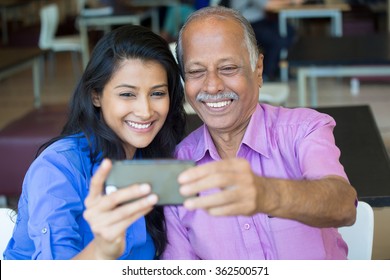 Closeup portrait happy elderly gentleman in pink shirt and lady in blue top taking selfie together, isolated indoors background. Say cheese and smile