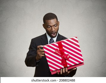 Closeup Portrait Happy Excited Surprised Young Businessman About To Open Unwrap Red Gift Box Isolated Grey Background, Enjoying His Present. Positive Human Emotions, Facial Expression Feeling Attitude