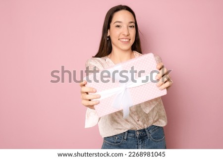 Close-up portrait of happy exited pretty brunette woman holding gift box, looking at camera, isolated on pink background