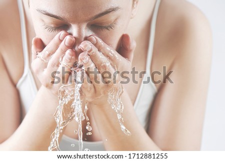 Close-up portrait of a happy girl washing her face with water splashes in white underwear. Fresh clean young female skin concept