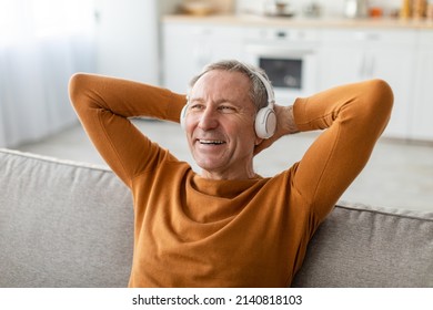 Closeup Portrait Of Happy Mature Man Listening To Music Wearing Wireless Headphones And Holding Hands Behind Head Sitting On Couch At Home. Senior Male Relaxing Resting On Sofa Enjoying Favorite Song - Shutterstock ID 2140818103