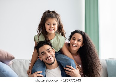 Closeup Portrait Of Happy Middle Eastern Parents And Their Cute Little Daughter Bonding Together At Home, Cheerful Arab Mom, Dad And Child Having Fun In Living Room, Laughing And Looking At Camera - Shutterstock ID 1967771743