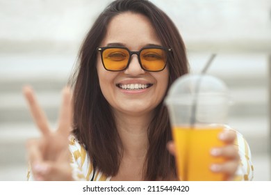 Closeup Portrait Of Happy Millennial Plus Size Woman 30-35 Years Old Smiling With White Teeth. Laughing Overweight Female In Orange Sunglasses Drinks Juicy Coctail In Summer Day