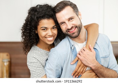 Close-up portrait of happy multi-ethnic couple in love. An African woman hugs a caucasian guy from behind, they looks at the camera with a cheerful smiles - Shutterstock ID 1911366292