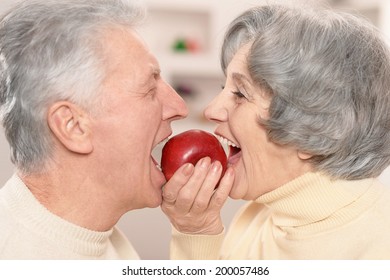 Close-up portrait of a happy senior couple eating apple at home