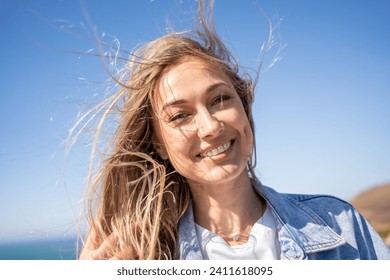 Closeup portrait of happy smiling beautiful woman with blond windswept hair. Cheerful female tourist on sea shore against blue sky. Lady enjoys summer vacation. - Powered by Shutterstock