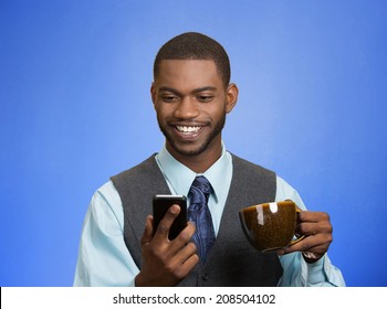 Closeup portrait happy, smiling business man reading good news on smart phone, lawyer holding mobile, drinking cup coffee isolated blue background. Human face expression, emotion, corporate executive 