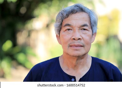 close-up portrait of happy and smiling  senior man with delicate facial features looking at camera while standing outside in front of his home in the garden with green environment.A male older than 60