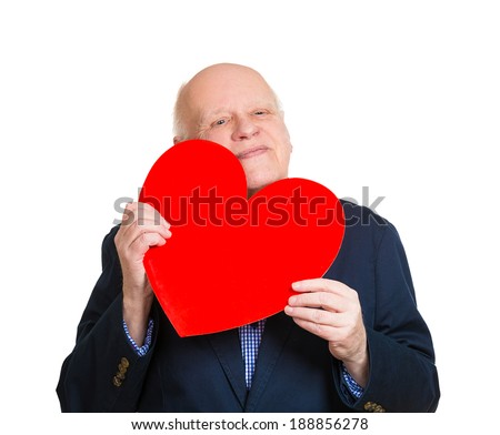 Closeup portrait, happy smiling, senior mature man looking at you, holding large red heart to chest daydreaming of women in love, isolated white background. Positive emotion facial expression feeling