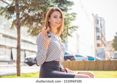 Closeup portrait happy, smiling, young attractive woman, buyer near her new car showing key isolated outside dealer, dealership lot office. Personal transportation, auto purchase concept